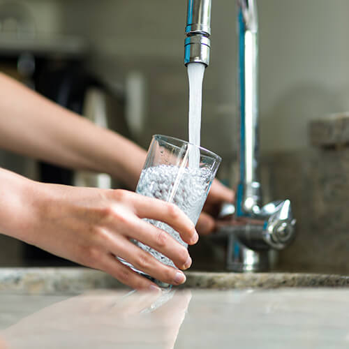 person filling up glass of clean drinking water that comes from a replaced water filter