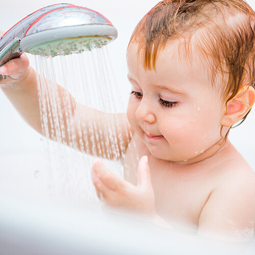 baby in tub playing with shower head
