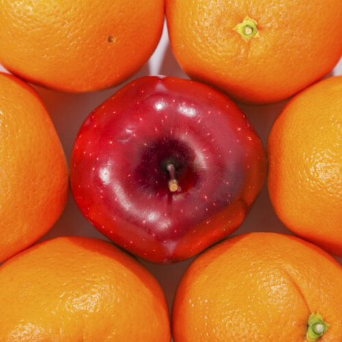 red apple surrounded by and standing out from oranges