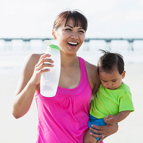 woman holding child & bottle of water because she knows what causes heatstroke & how water can help prevent it
