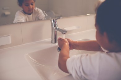 6 years, mixed-race girl washing her hands with soap in the white sink under the tap running water. Hygiene and a healthy lifestyle concept.