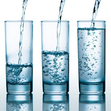 Transparent glasses with different level of water, pouring water into glasses