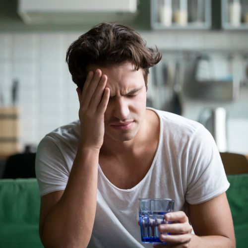 man suffering from migraine drinks water