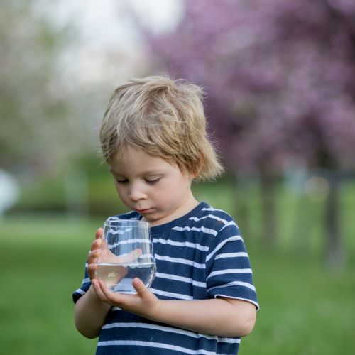 Boy outside looking at well water in a glass.