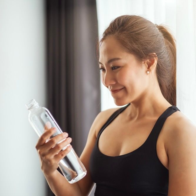 A beautiful asian woman holding and looking at a water bottle while working out